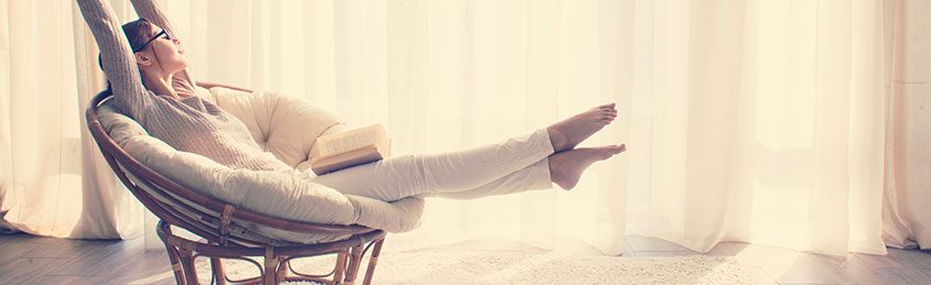 Une femme portant des lunette se relaxe sur un sofa design circulaire avec un livre ouvert sur les jambes. Un rideau avec une lumière calme en fond